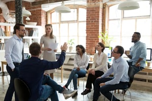 Un groupe de professionnels est assis autour d'un bureau, engagé dans une conversation. Leurs ordinateurs portables sont ouverts, mais ils sont tournés loin des écrans, soulignant l'importance de l'interaction humaine.