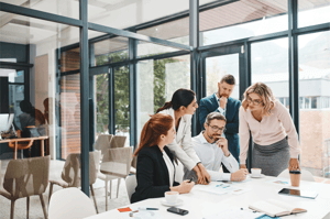 Un groupe de professionnels se tient autour, regardant très sérieusement des documents ensemble, indiquant une discussion ou une collaboration concentrée. Leurs expressions reflètent la concentration et l'engagement envers le contenu.